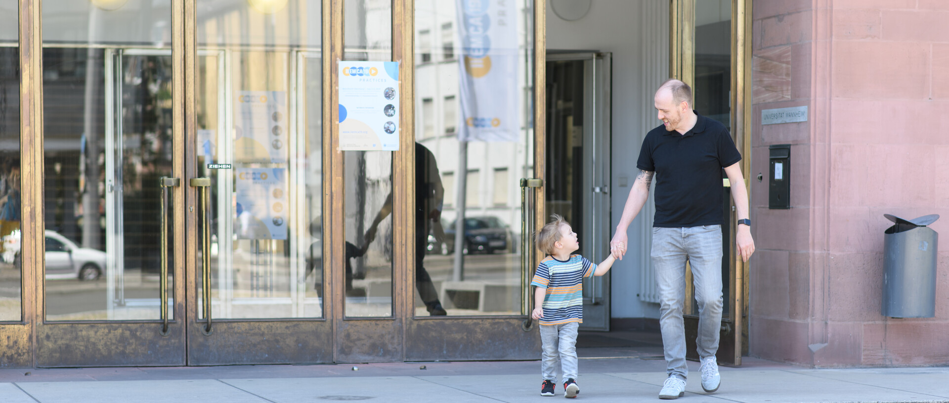 Vater und Sohn gehen Hand in Hand aus der Universität Mannheim.