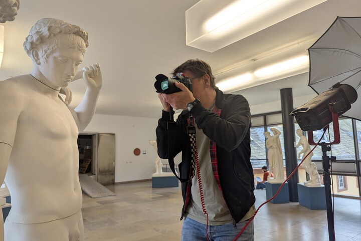 Grafiker Ulrich Ambach fotografiert die Statuen im Antikensaal. Er hält eine große Kamera vor sein Gesicht.