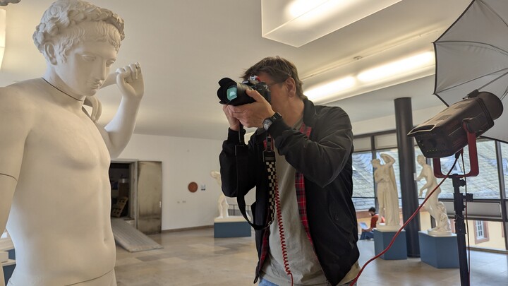 Grafiker Ulrich Ambach fotografiert die Statuen im Antikensaal. Er hält eine große Kamera vor sein Gesicht.