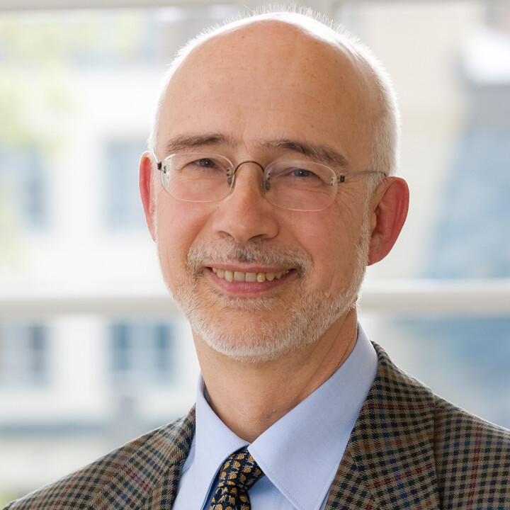 Portrait von Thomas Puhl. Er lächelt und trägt einen dunkelbraun karrierte Blazer sowie eine Krawatte.