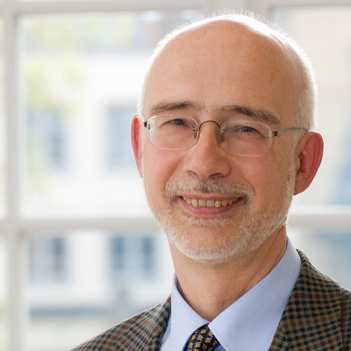 Portrait von Thomas Puhl. Er lächelt und trägt einen dunkelbraun karrierte Blazer sowie eine Krawatte.