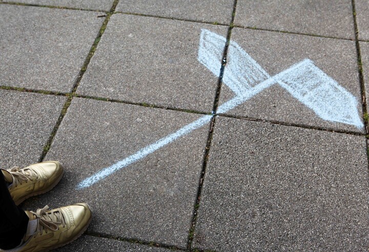 Auf dem Boden ist mit Kreide ein Wegweiser gemalt. Ein Pfeil zeigt nach rechts der andere nach links.