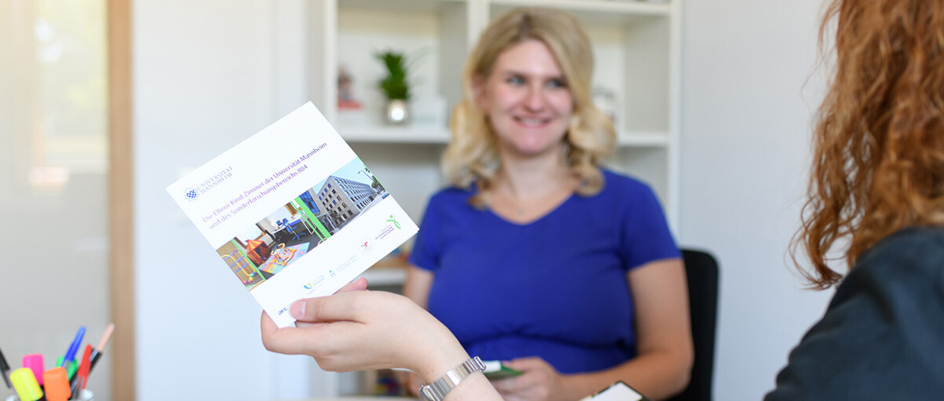 Schwangere Frau lächelt und spricht mit einer anderen Frau, die sie berät