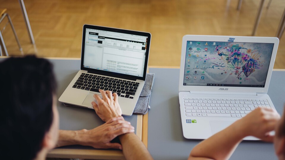 Zwei Studierende sitzen an einem Tisch und schauen auf ihre Laptop-Bildschirme