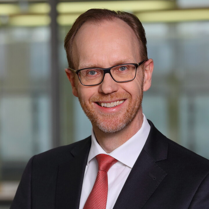 Prof. Dr. Lobin im Porträt mit schwarzem Anzug, weißem Hemd, roter Krawatte und schwarzer rechteckiger Brille in einem Büro