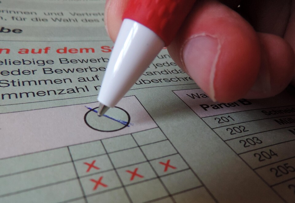 Eine Person macht auf einem Wahlschein ein Kreuz.
