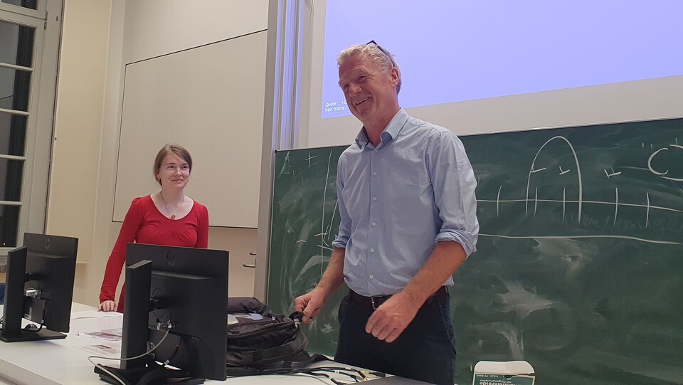 Thomas Koenig und Anna Maria Rohe stehen nebeneinander hinter einem Pult vor einer Kreidetafel.