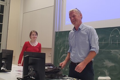 Thomas Koenig und Anna Maria Rohe stehen nebeneinander hinter einem Pult vor einer Kreidetafel.