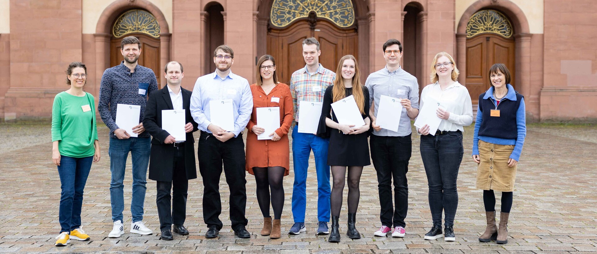 Lehr­ende, Mitarbeitenden und Studierende stehen mit ihren Zertifikaten zur Hochschuldidaktik auf dem Ehrenhof.