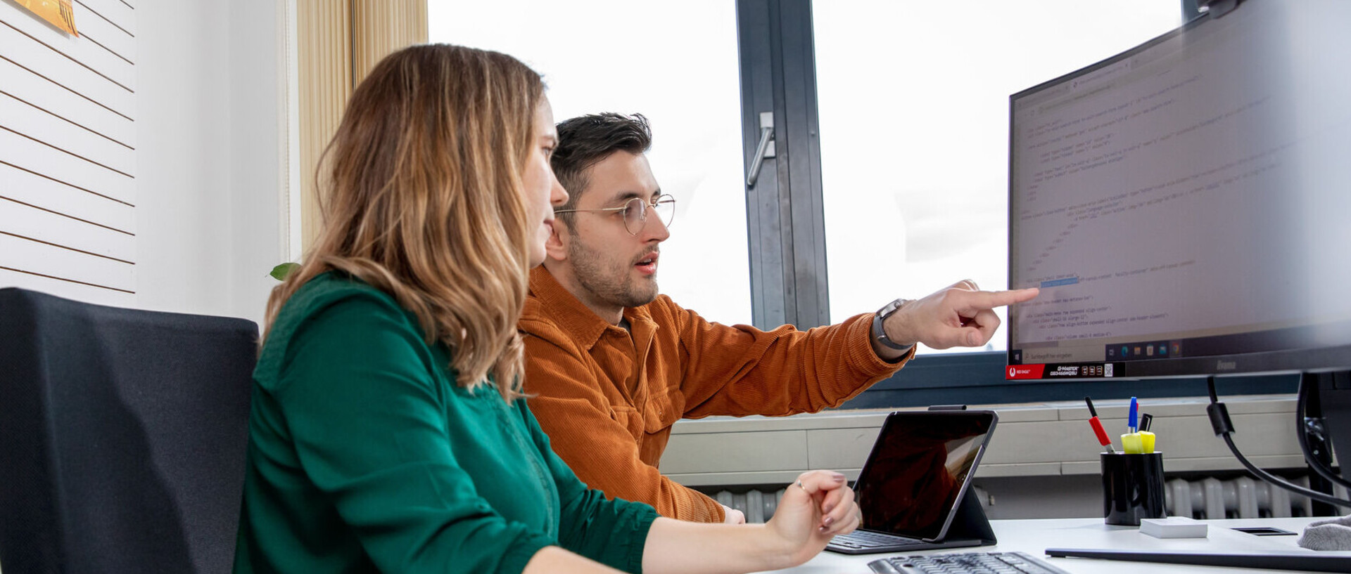 Zwei Mitarbeitende der IT vor einem großen Bildschirm.