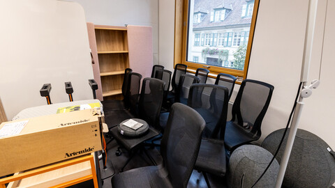 Zu sehen ist die Ecke eines Raumes in der viele verschiedene Möbelstücke zusammengestellt sind, Bürostühle, Regale, Tische und Design-Steckdosen