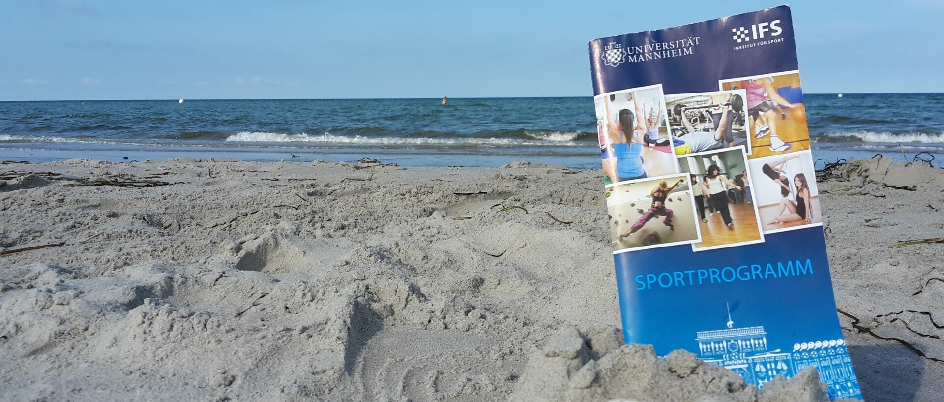 Sportprogrammbroschüre liegt im Sandstrand am Meer
