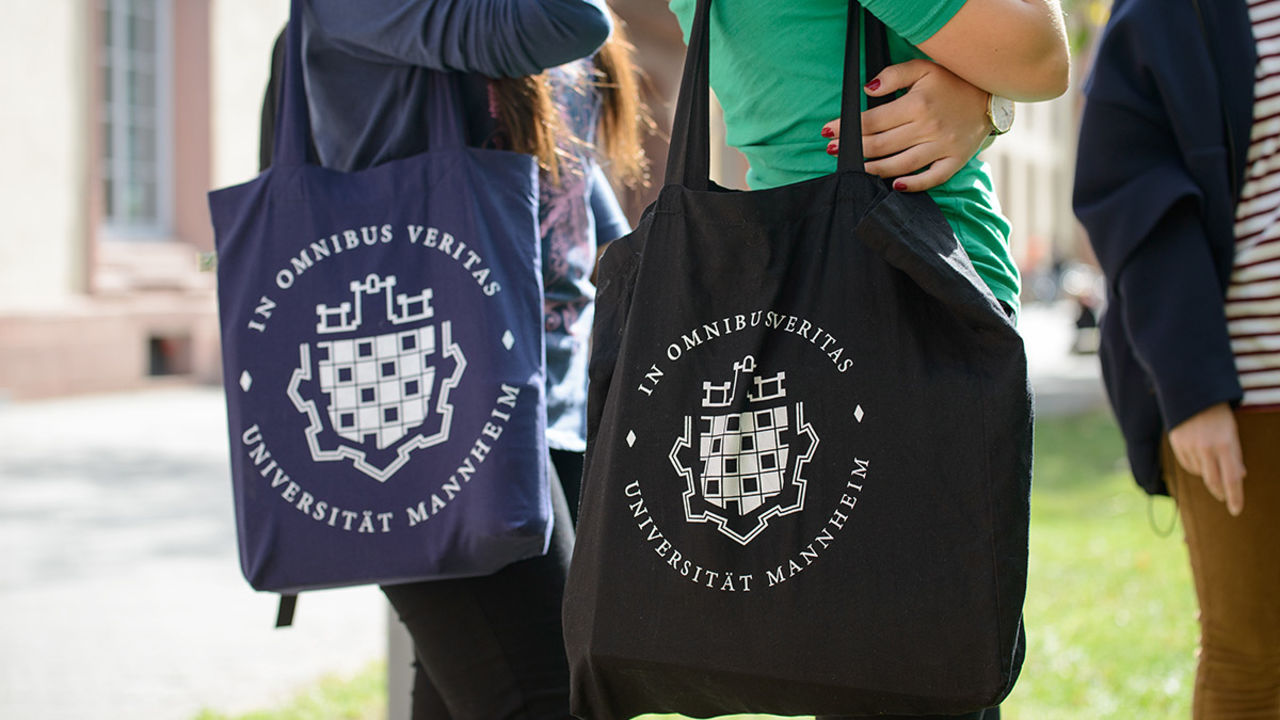 Zwei Studentinnen tragen Jutebeutel mit dem Logo der Universität Mannheim.