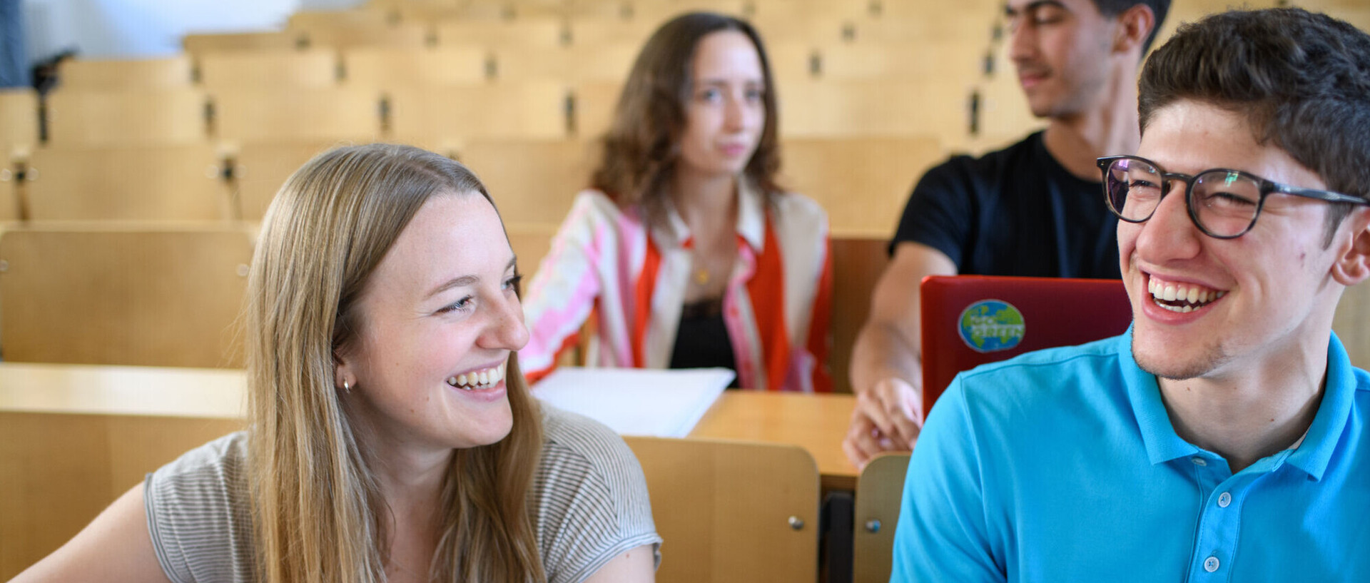 Studierende sitzen lachend in einem Vorlesungsraum