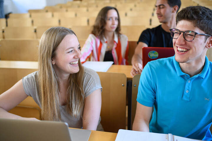 Studierende sitzen lachend in einem Vorlesungsraum 
