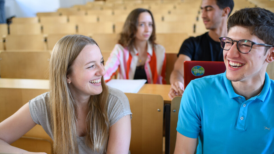 Studierende sitzen lachend in einem Vorlesungsraum