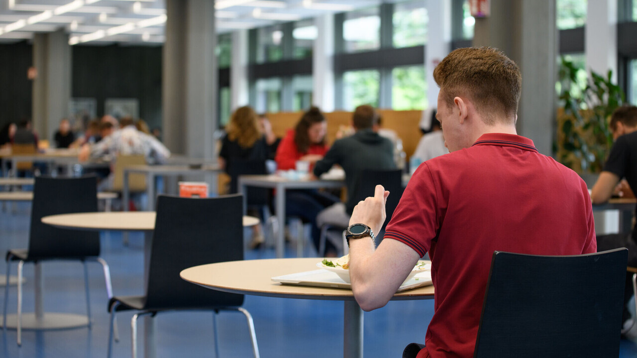 Mensa at the Schloss Ein Student in rotem Tshirt sitzt in der Mensa an einem Tisch und isst zu Mittag.