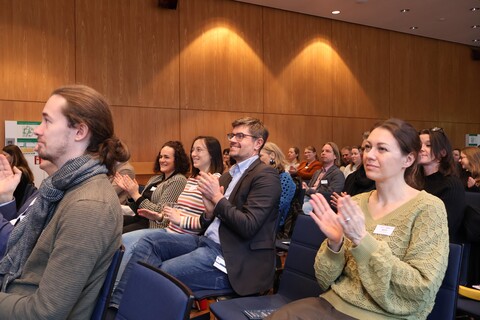 Applaudierendes Publikum in einem holzvertäfelten Raum.