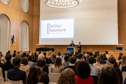 Die Gäste der Feier sitzen in der Aula während vorne eine Rede gehalten wird 