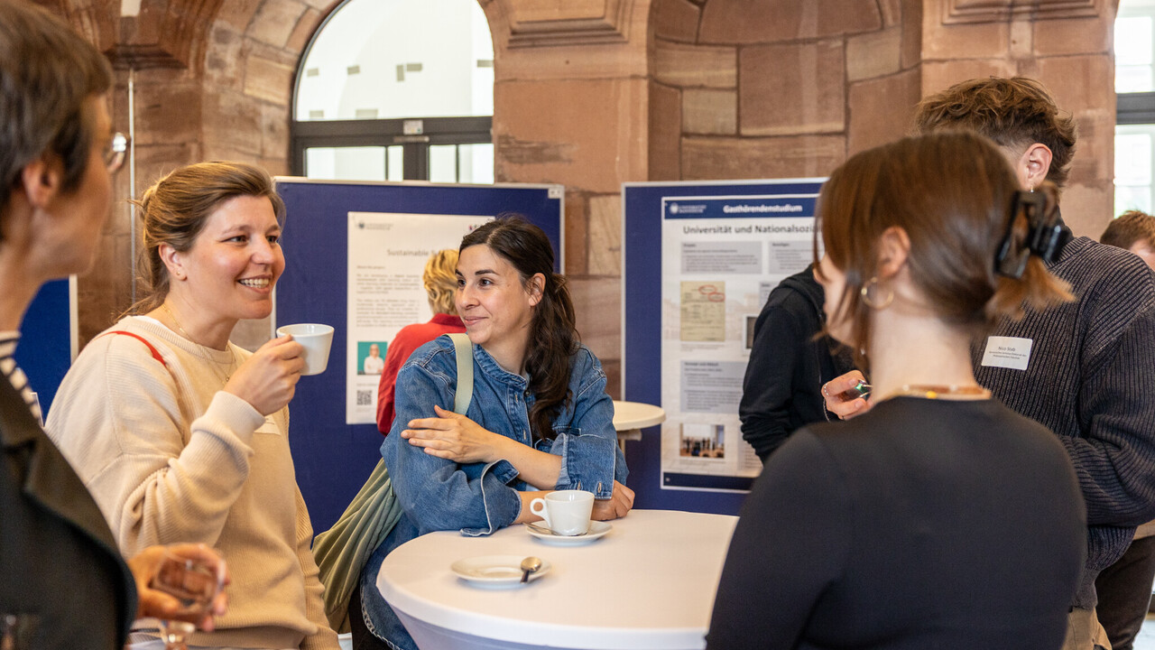 Lockere Runde an einem Stehtisch in den Katakomben des Schlosses: Personen im Gespräch, im Hintergrund Poster auf Stellwänden.