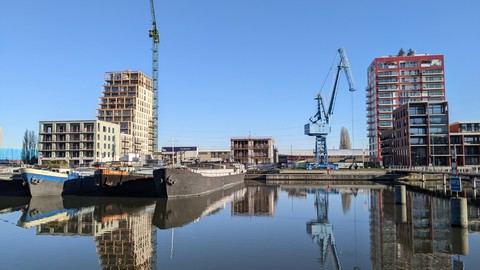 An einem Kanal werden Gebäude erbaut. Zwei Kräne stehen in der Mitte.