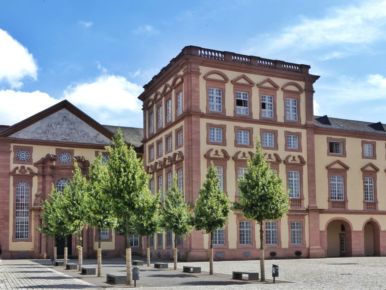 Der Kunstturm und der Ehrenhof Ost im Sonnenlicht. Davor grün belaubte Bäume.