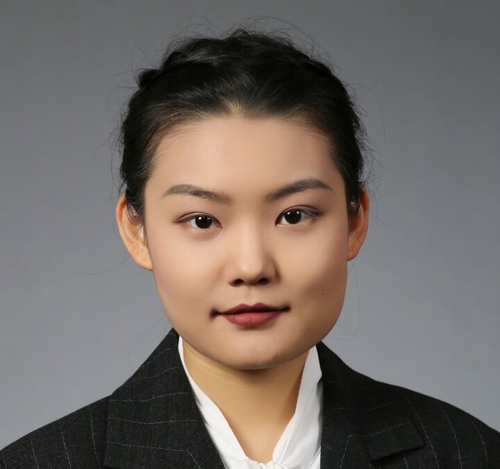 Yue Wu. She is wearing a black suit and is standing in front of a grey wall.