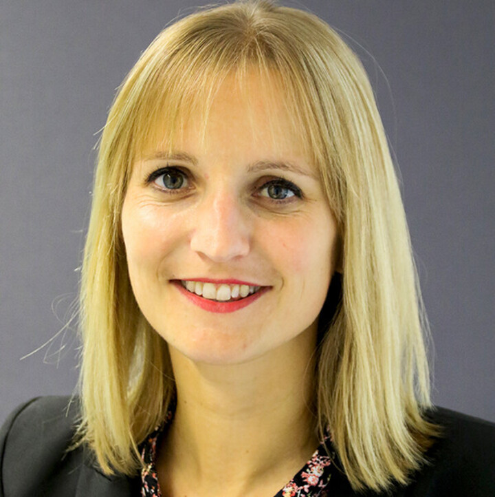 Portrait einer Frau mit blonden Haaren vor einem grauen Hintergrund.