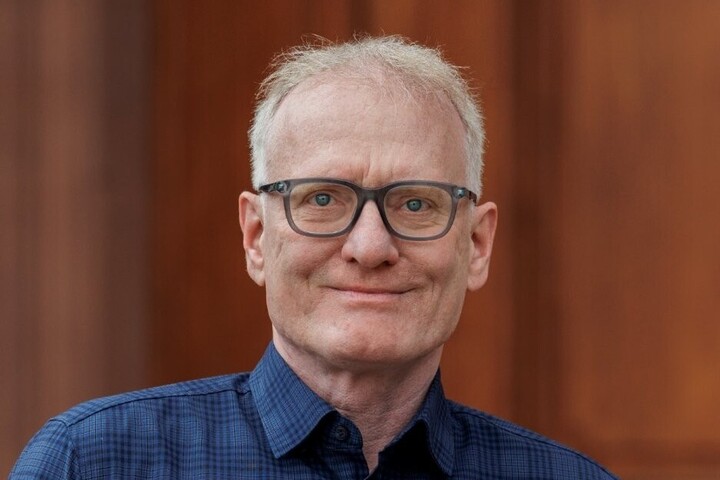 Matthias Kohring blickt direkt in die Kamera. Er hat eine Brille und trägt ein blau-kariertes Hemd