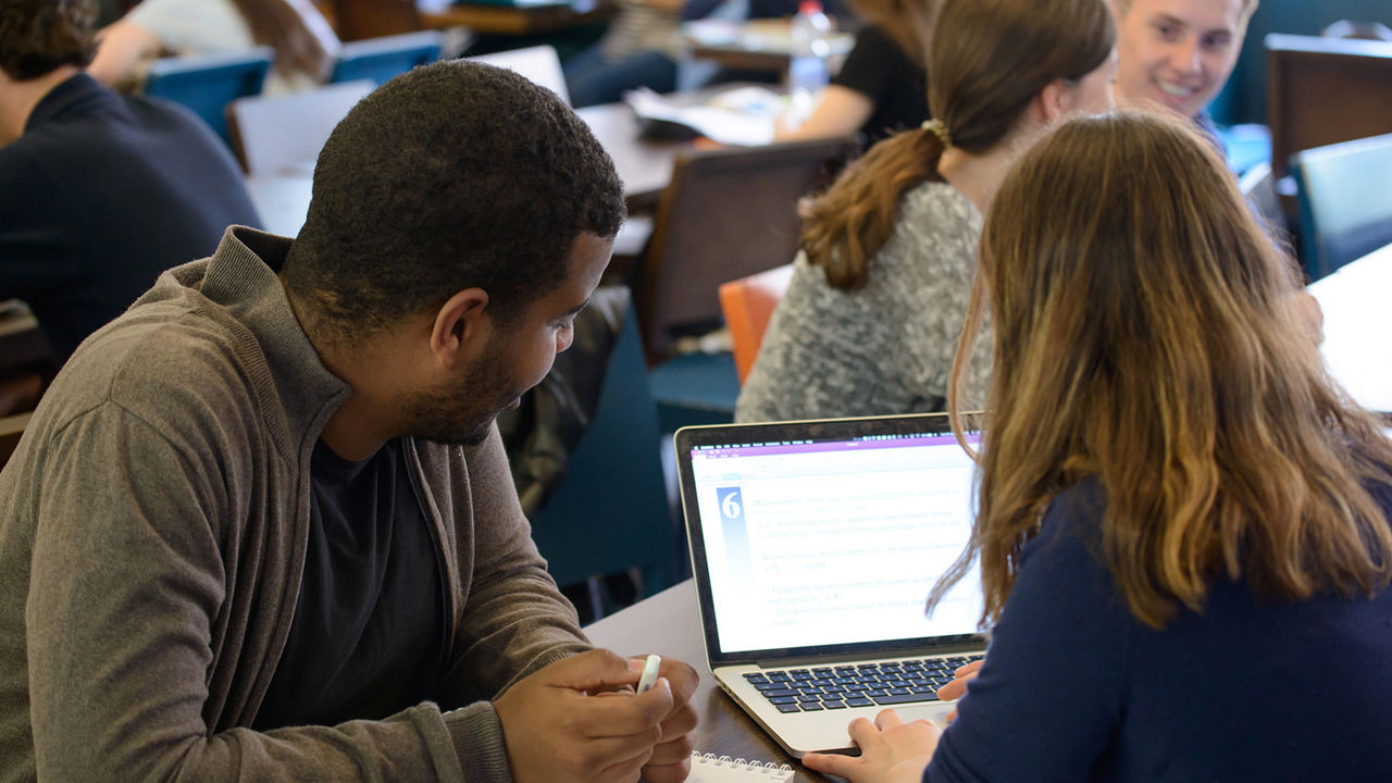 Ein Student und eine Studentin sitzen an einem Tisch und lernen zusammen. Sie schauen gemeinsam auf einen Laptop.