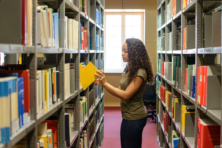 Studentin zieht aus dem Regal in der Bibliothek ein Buch