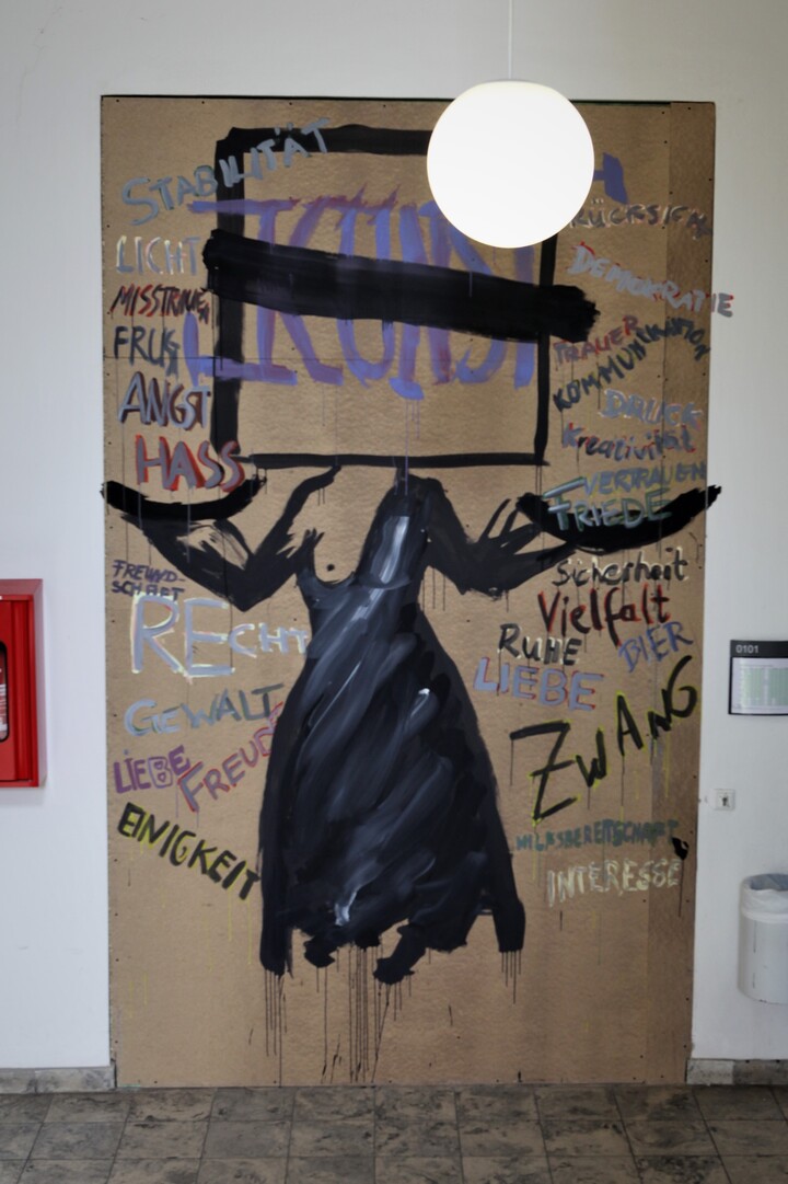 Kunstwerk mit einem schwarzen Kleid im Zentrum. Drum herum stehen in verschiedenen Farben unterschiedliche Substantive geschrieben. Über dem Kleid steht schwarz eingerahmt und einfach durchgestrichen in großen Buchstaben der Begriff"Kunst"