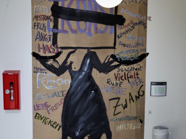 Kunstwerk mit einem schwarzen Kleid im Zentrum. Drum herum stehen in verschiedenen Farben unterschiedliche Substantive geschrieben. Über dem Kleid steht schwarz eingerahmt und einfach durchgestrichen in großen Buchstaben der Begriff"Kunst"