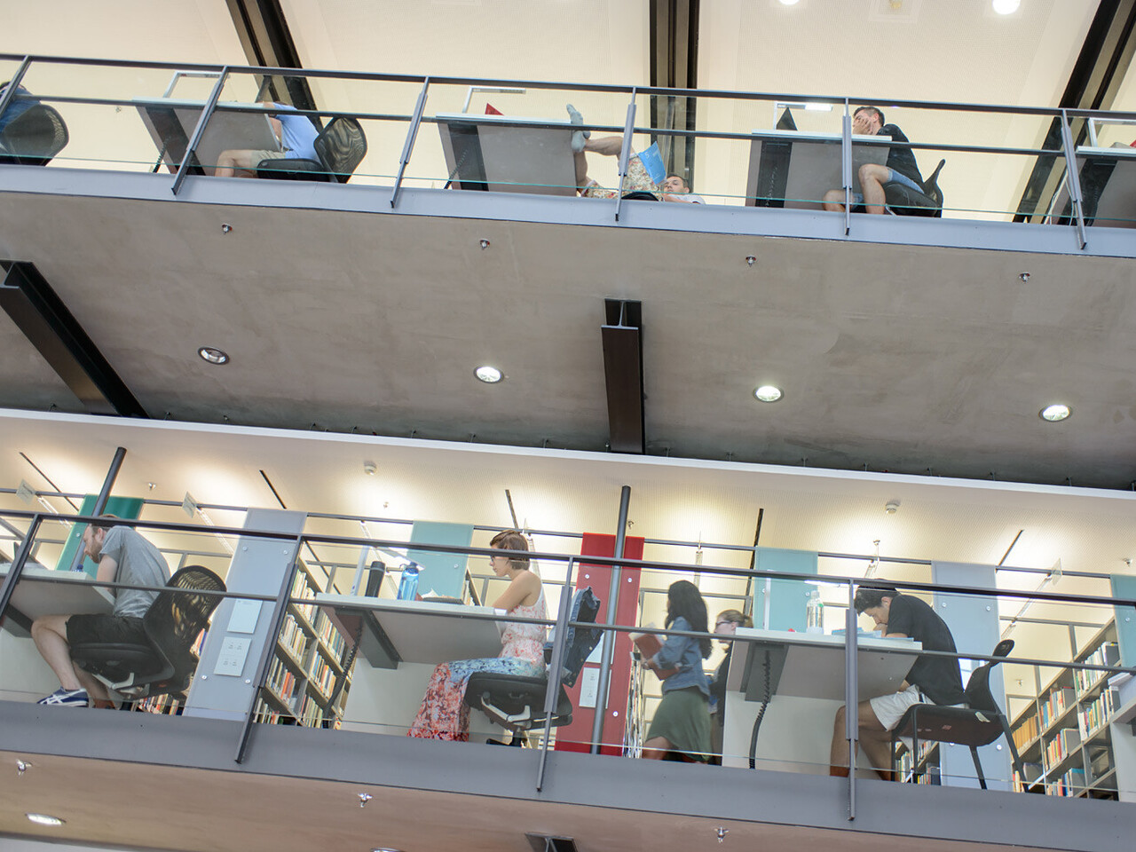 Students in the library Studierende sitzen auf verschiedenen Etagen der Bibliothek an Arbeitsplätzen.