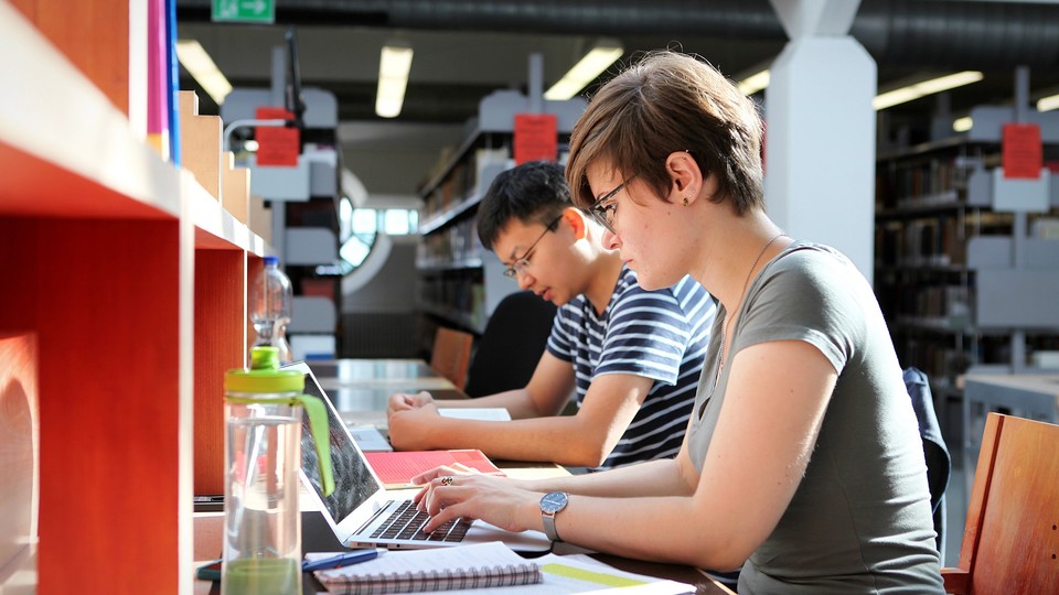 Eine Studentin und ein Student sitzen in der Bibliothek nebeneinander und lernen.