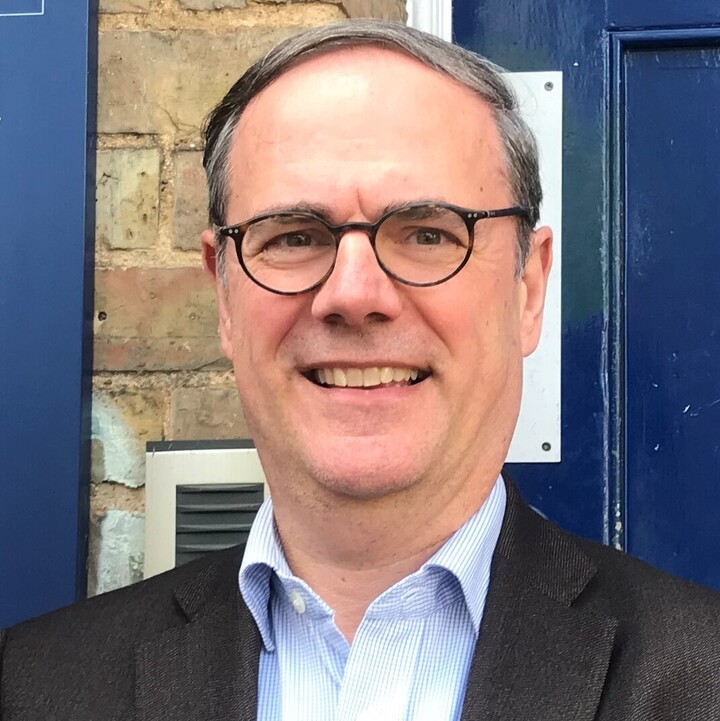 Prof. Dr. Ebbinghaus trägt ein hellblaues Hemd und ein dunkles Sakko und steht vor der blauen Haustür des Barnett House, Zentrum für evidenzbasierte Intervention der Universität Oxford