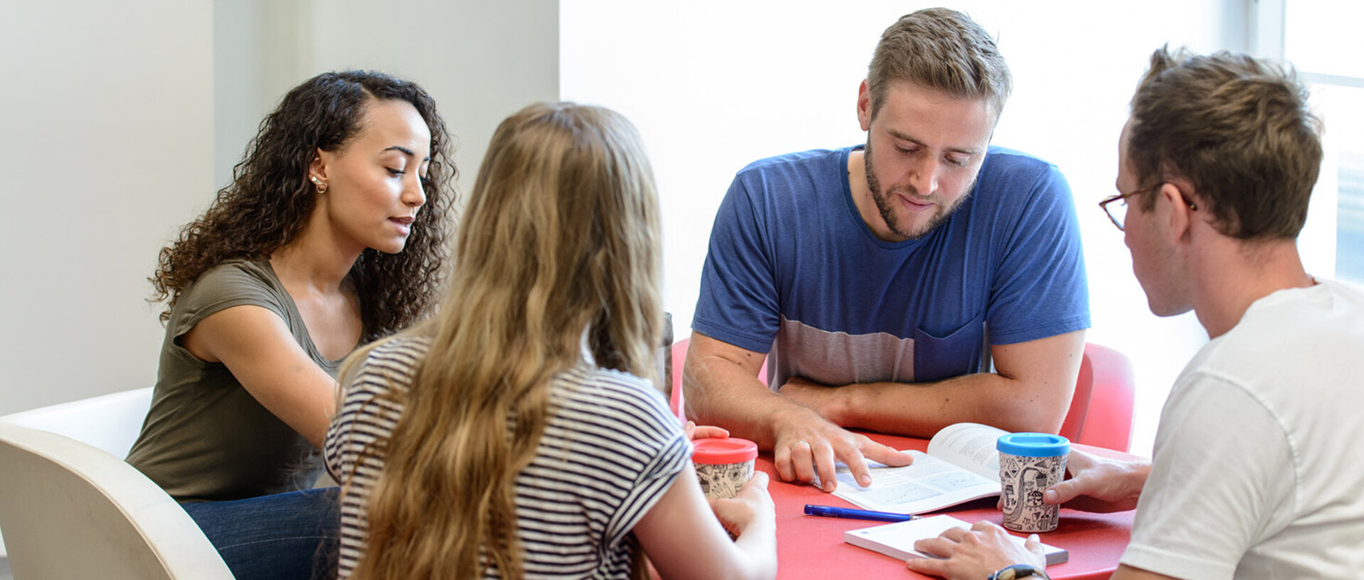 Vier Studierende sitzen an einem runden Tisch und lernen gemeinsam.