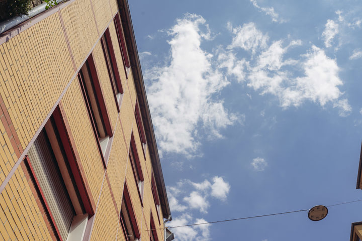 Eine Fassade aus gelbem Stein aus der Froschperspektive. Der Himmel ist blau und hat ein paar weiße Wolken.