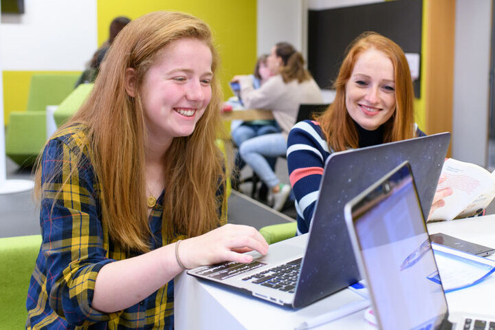 Zwei Studentinnen blicken lachend auf einen Laptop.