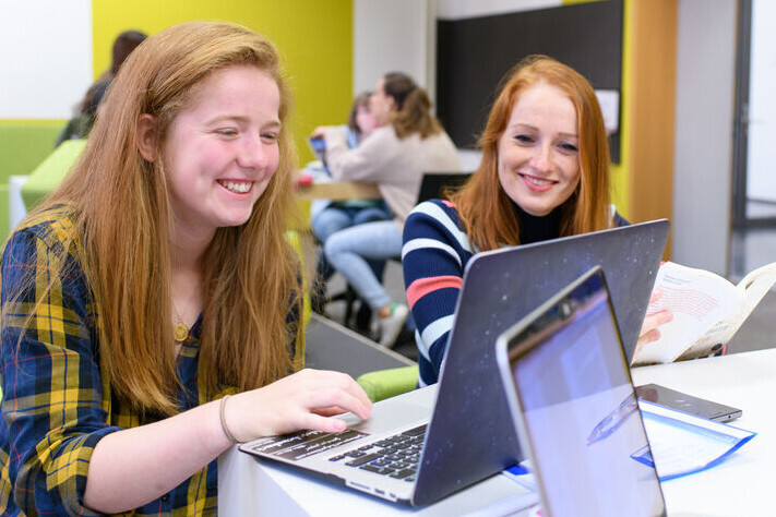 Zwei Studentinnen blicken lachend auf einen Laptop.