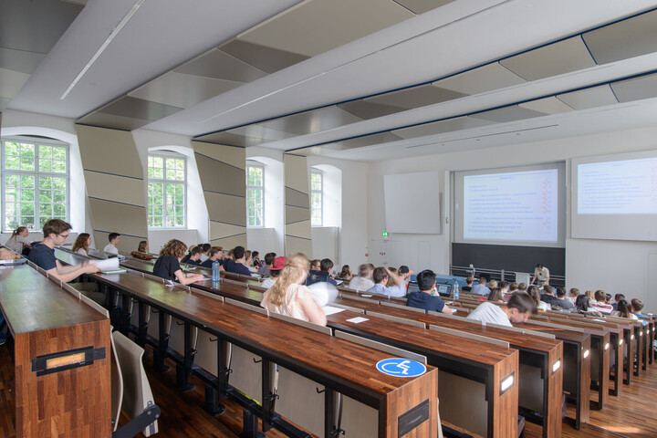 Studenten sitzen in einem Hörsaal und ein Professor hält eine Vorlesung.