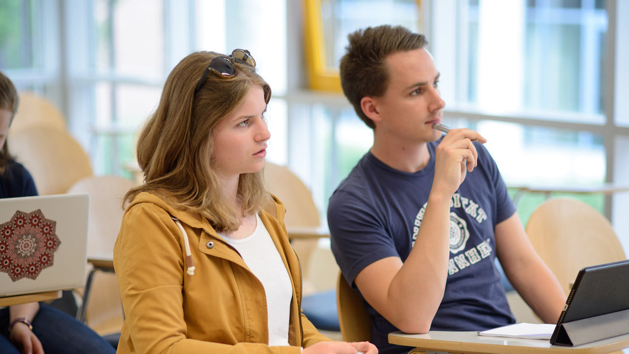 Zwei Studierende sitzen nebeneinander. Sie schauen konzentriert nach vorne.