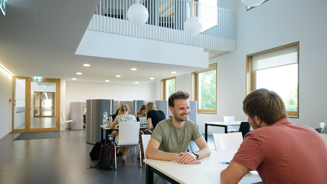 Zwei Studenten sitzen gemeinsam an einem Tisch im Gebäude B6 der Universität Mannheim.