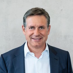 Alexander Schwörer trägt ein weißes Hemd mit blauem Sakko. Er hat kurze Haare, braune Augen und lächelt freundlich.