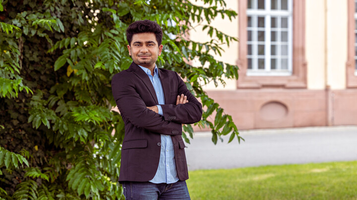 Shivam Suchak steht vor einem Busch auf dem Mannheimer Campus und verschränkt die Arme.