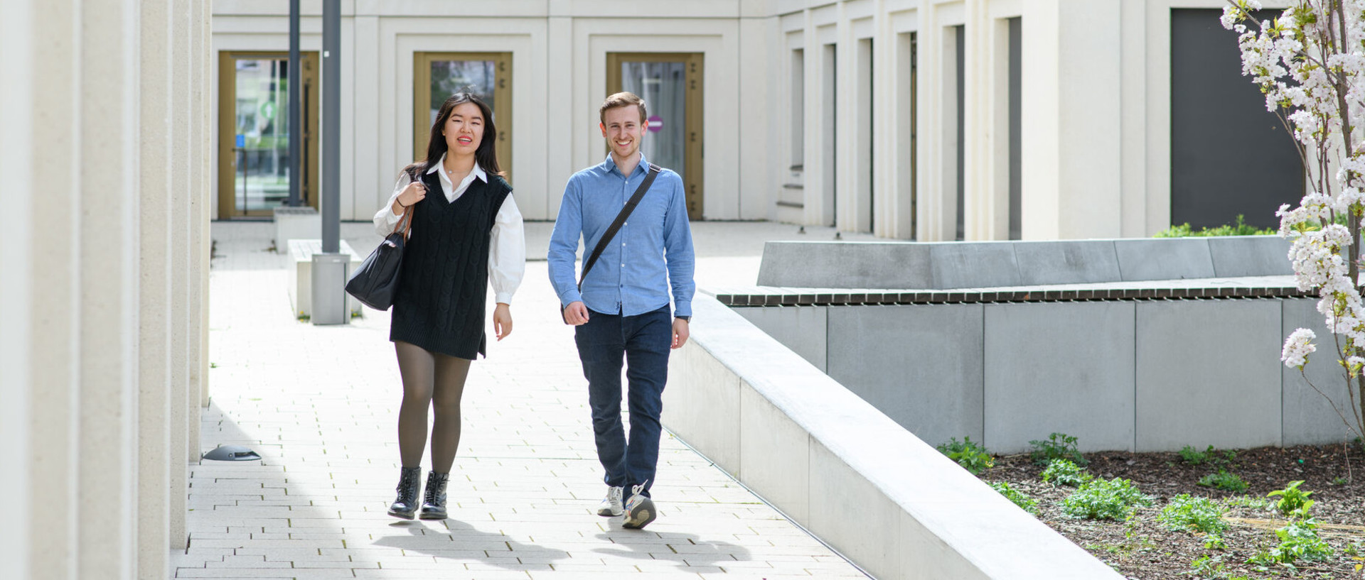 Eine Studentin und ein Student laufen lachend nebeneinander im Innenhof des B6-Gebäudes der Universität Mannheim entlang