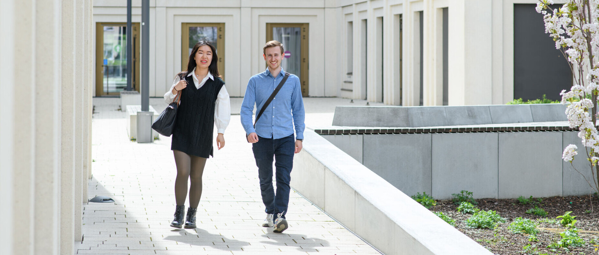 Eine Frau und ein Mann laufen lachend nebeneinander im Innenhof des B6-Gebäudes der Universität Mannheim entlang