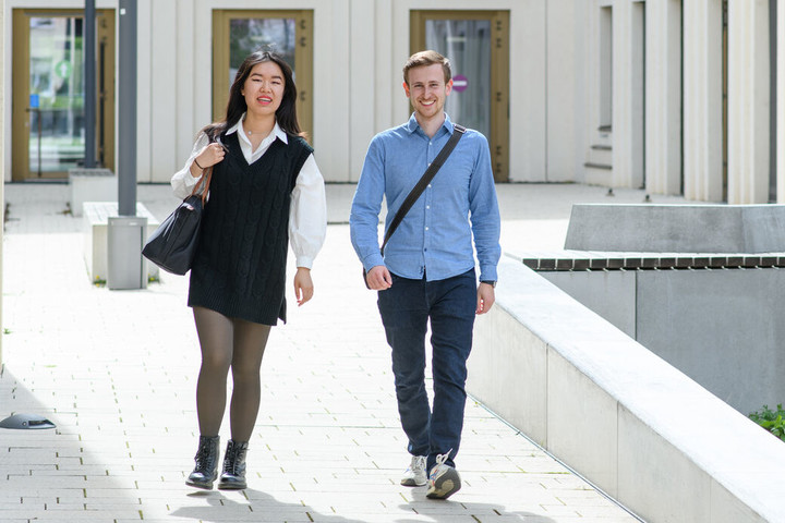 Eine Studentin und ein Student laufen lachend nebeneinander im Innenhof des B6-Gebäudes der Universität Mannheim entlang