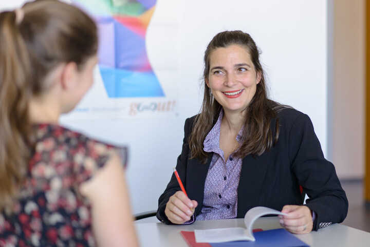 Eine lachende Mitarbeiterin berät eine junge Studentin in einem persönlichen Gespräch.