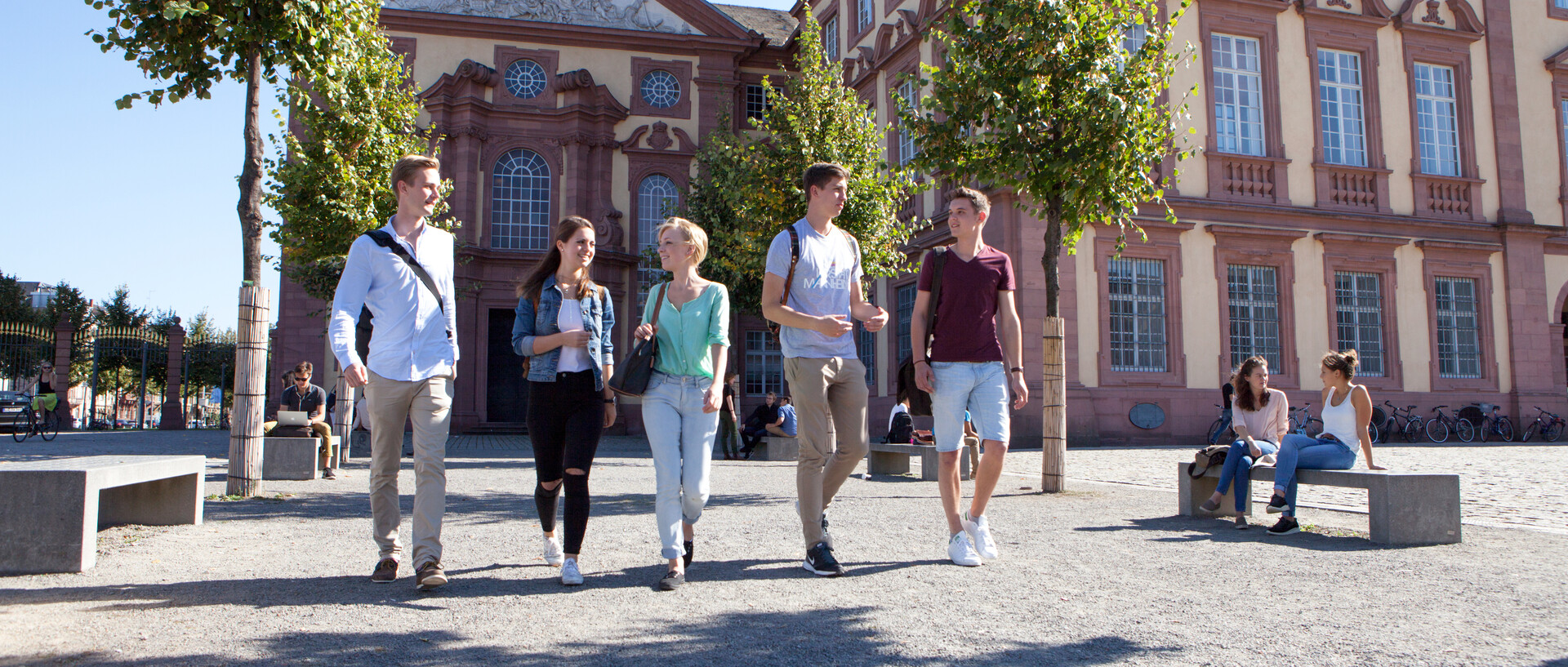 Students are walking across the Ehrenhof of the Mannheim Castle under the sunlight.